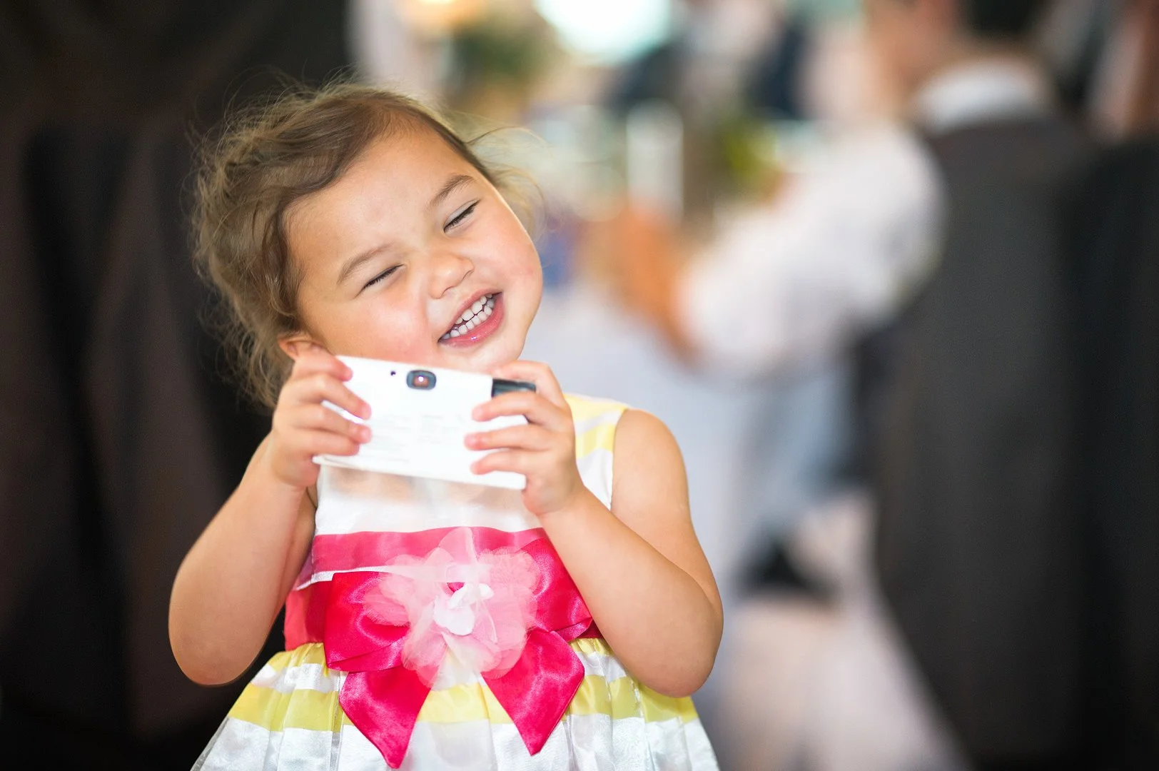 Little girl in red, white and yellow party dress takes a photo on her camera during a wedding breakfast at The Lowry.