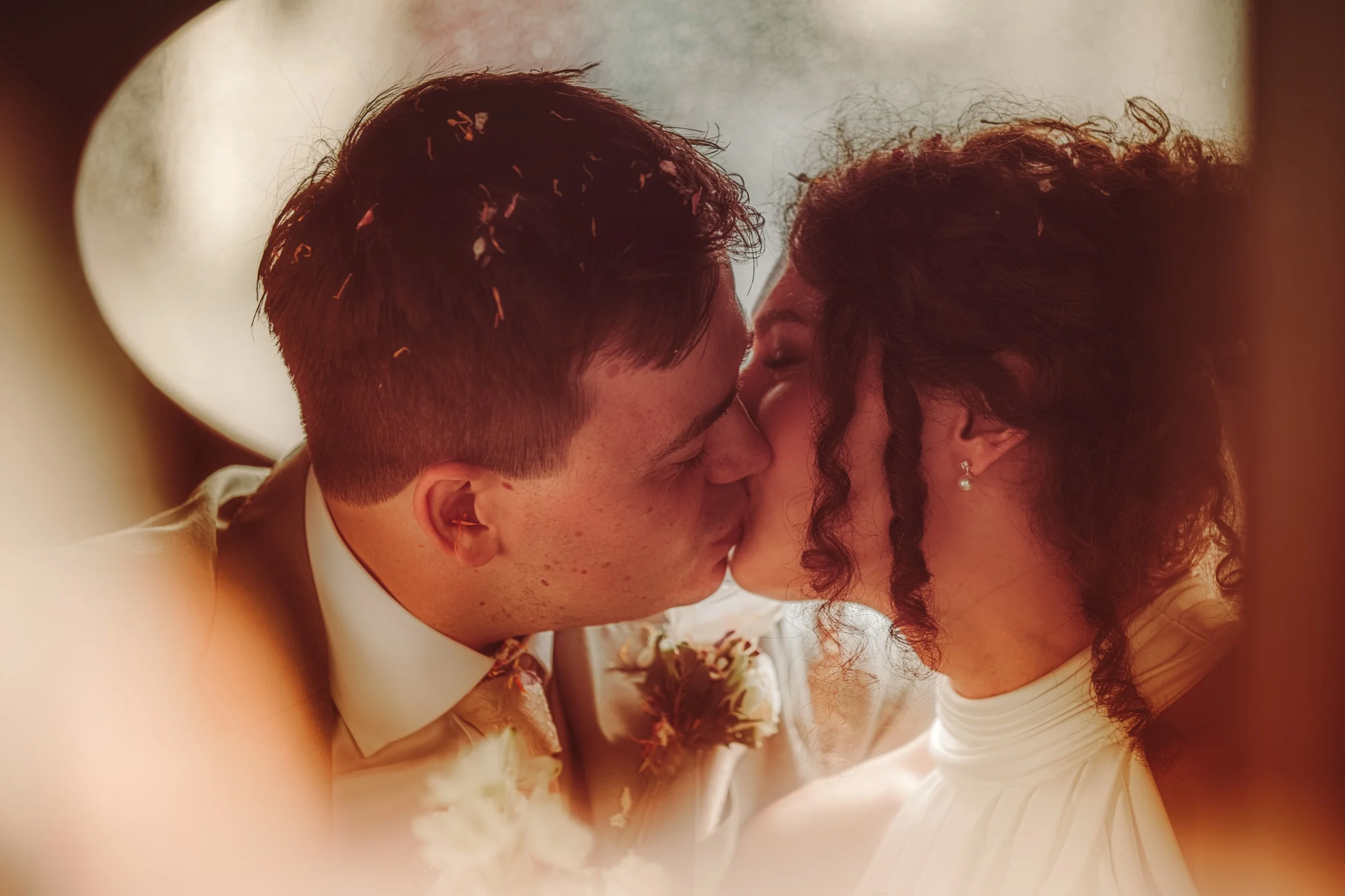 A couple sharing a close, intimate moment with their foreheads touching, dressed in wedding attire, with the focus on their faces and the bride's earrings, with a soft, blurred background.
