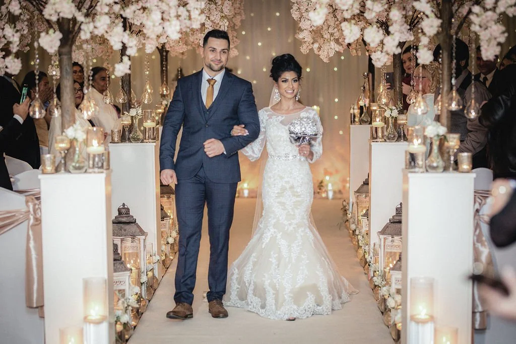 Bride and groom walking down the aisle at their wedding reception, surrounded by floral decorations and guests.