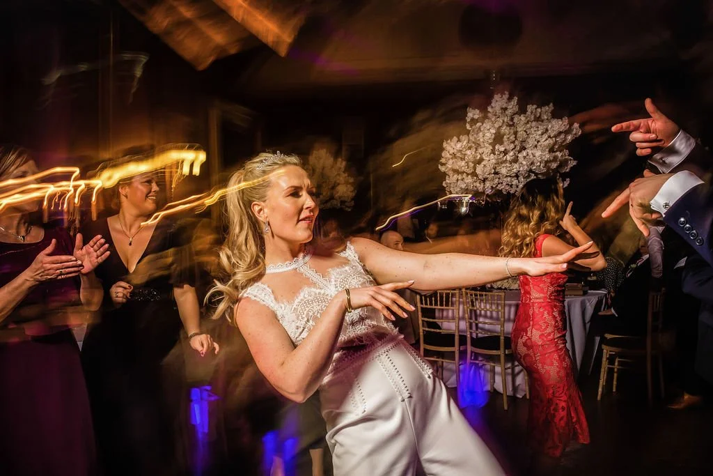 Women dancing at a wedding reception with glowing lights and floral decorations.