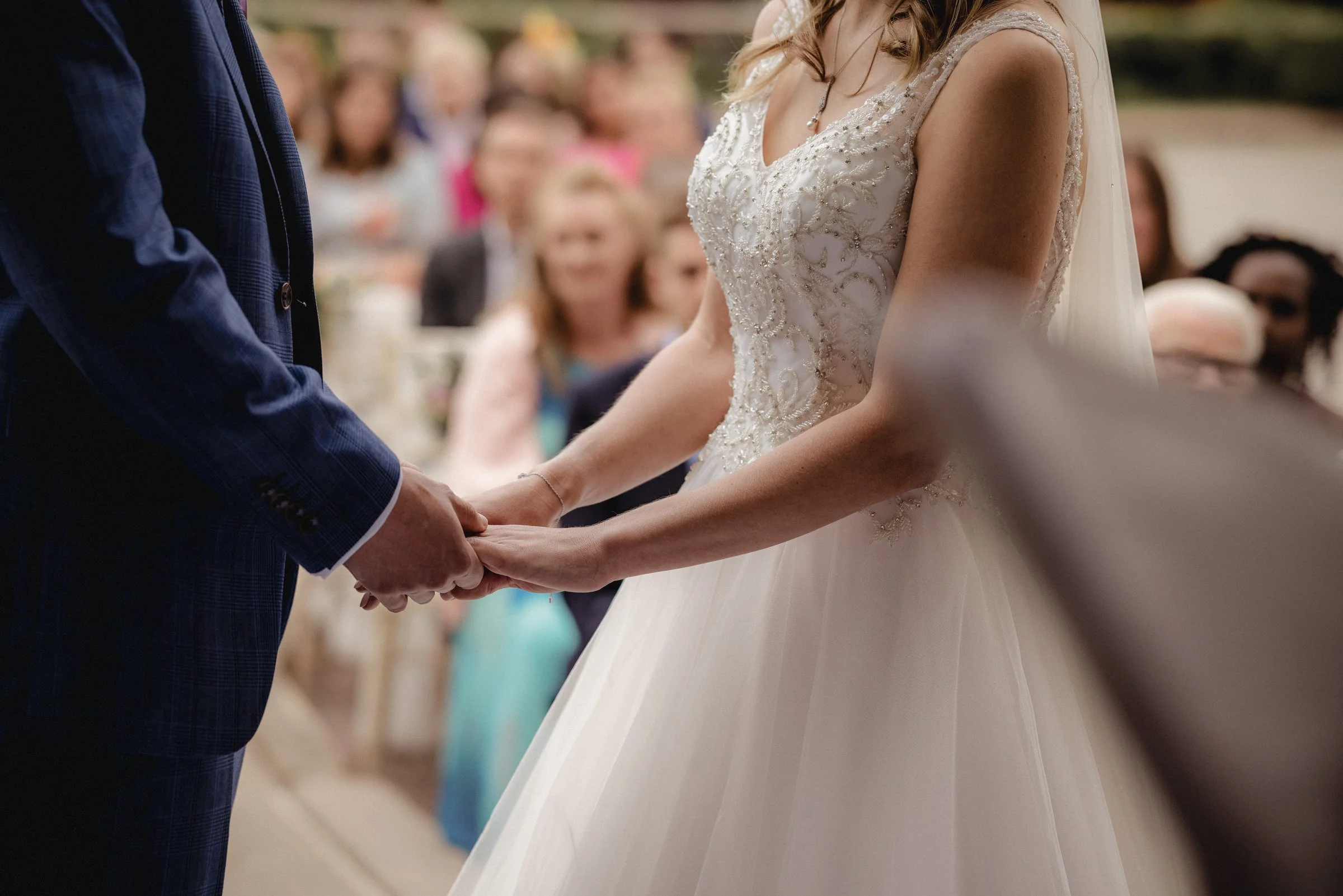 A bride and groom holding hands during a wedding ceremony, with guests seated in the background.