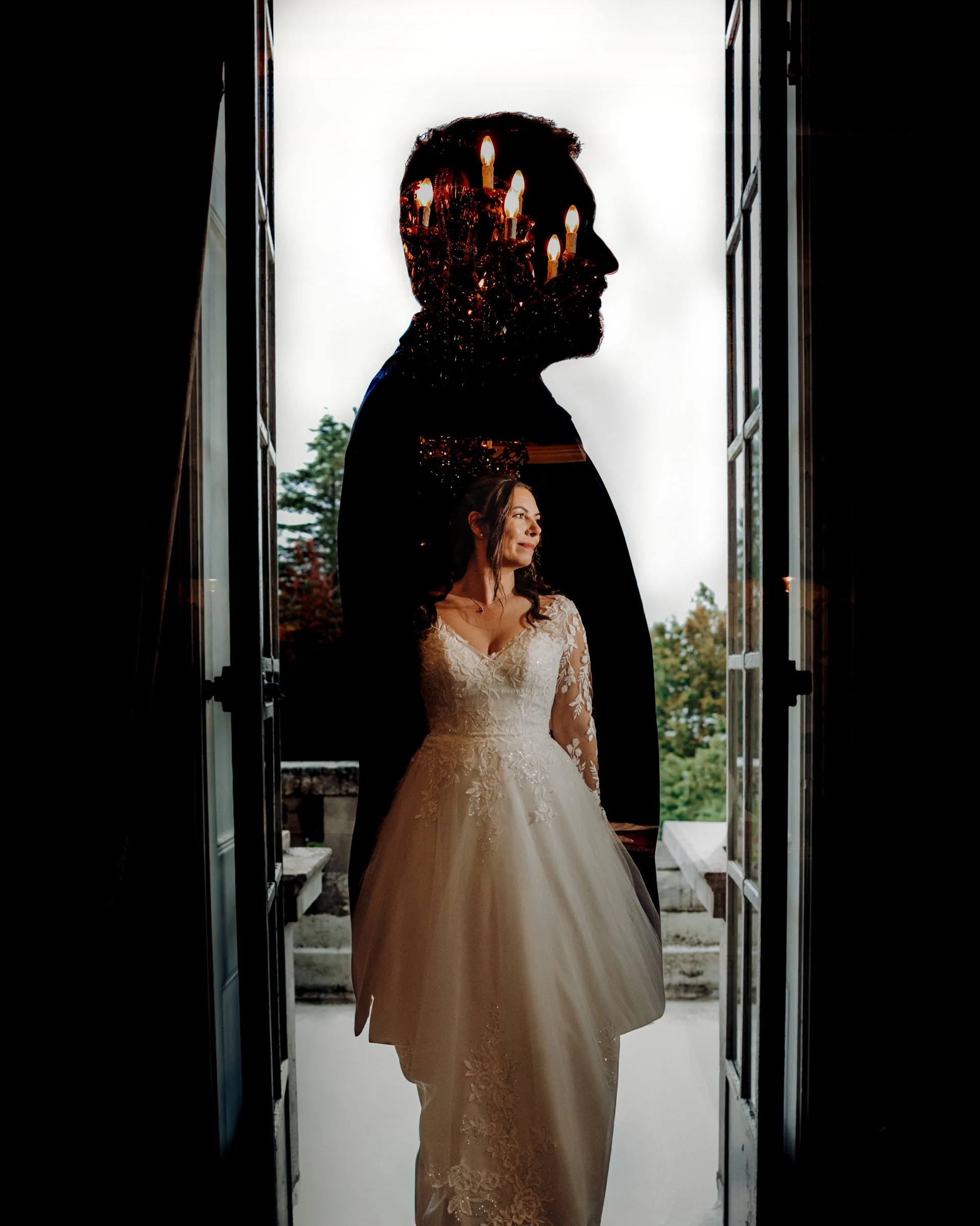 Double exposure image of bride in white dress set within silhouette of groom standing side on in open doorway with chandelier above brides head