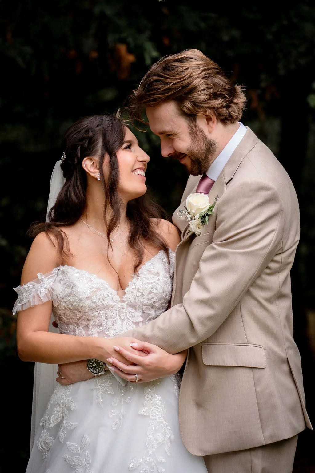 A bride and groom sharing a joyful moment on their wedding day, smiling and looking into each other's eyes while holding hands.