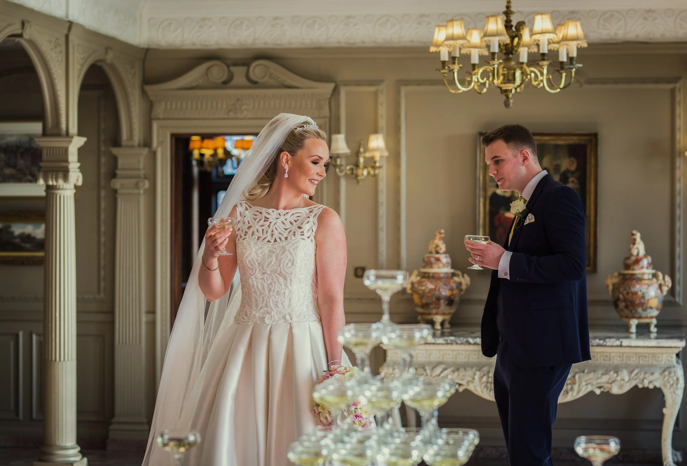A bride and groom celebrating with champagne at their wedding reception in an elegant, decorated room with ornate details and vintage decor.