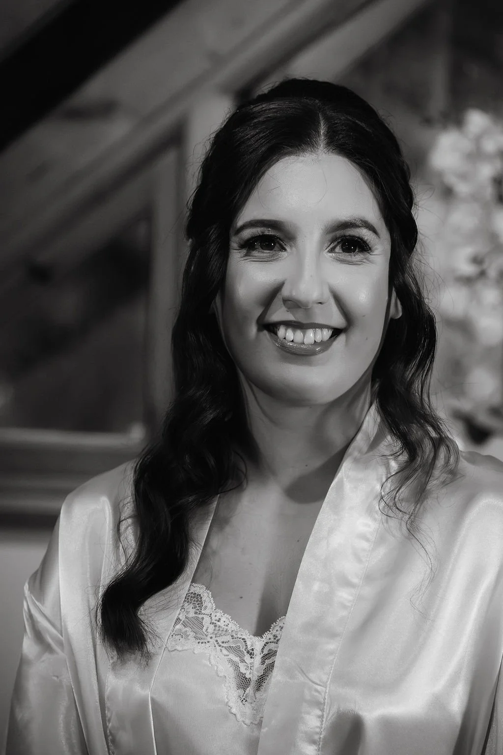 Black and white portrait of a smiling woman with long wavy hair, wearing a satin robe with lace detail.