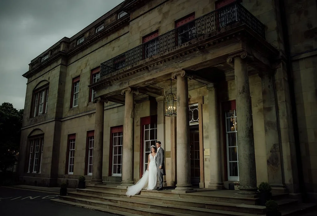 A bride and groom standing on the steps of a historic stone building with columns and a balcony.