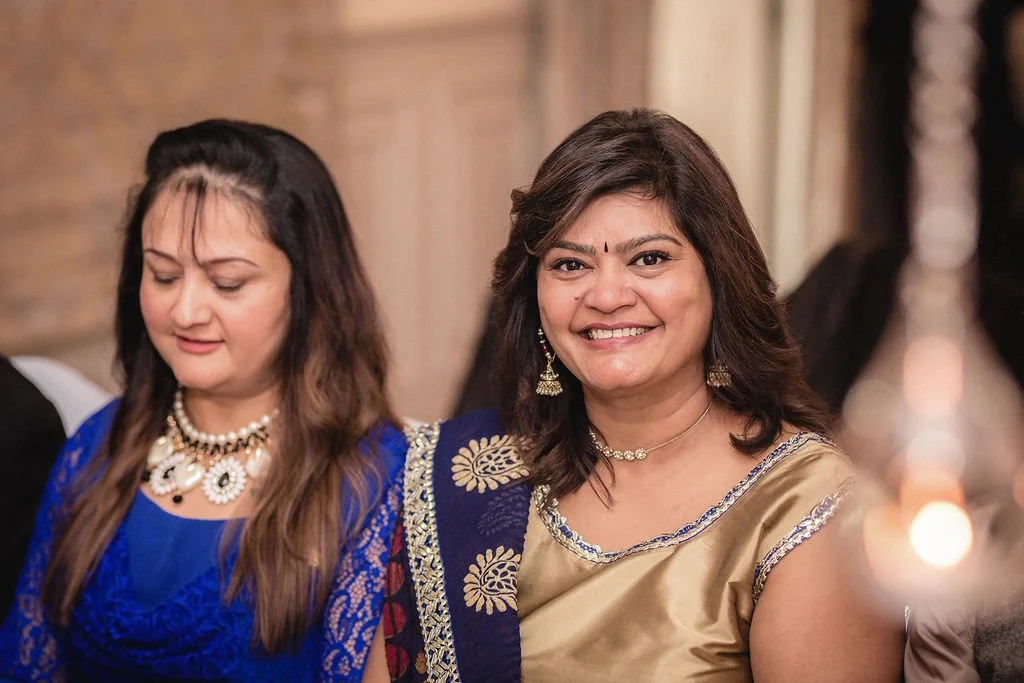 Two women smiling and dressed in traditional Indian attire at a celebration or gathering.