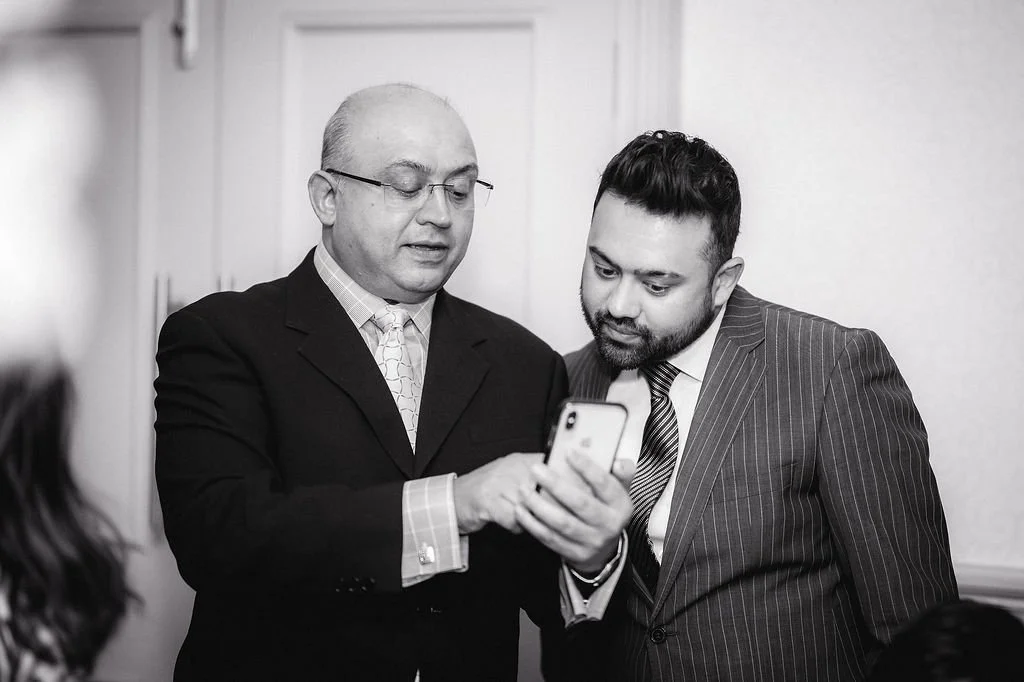 Two men in suits looking at a smartphone together in a room.