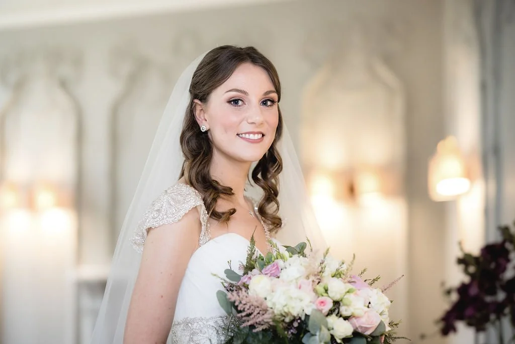 Bride in wedding dress holding a bouquet of flowers indoors, smiling.