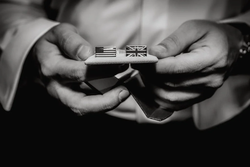 Close-up of hands holding a small box with two rings, one with an American flag design and the other with a British flag design.