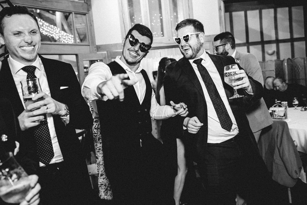 Group of men celebrating at a party, some wearing sunglasses and holding drinks, smiling and dancing.