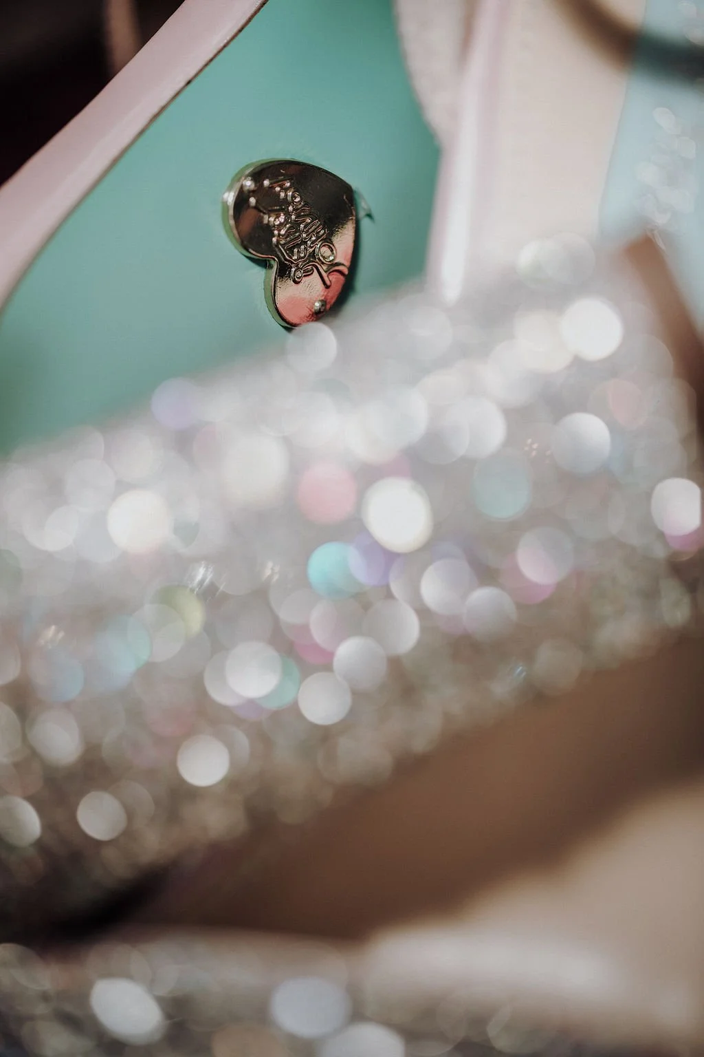 Close-up of a shiny silver button or part with a reflective surface on a pastel teal surface, with blurred multicolored bokeh lights in the foreground.