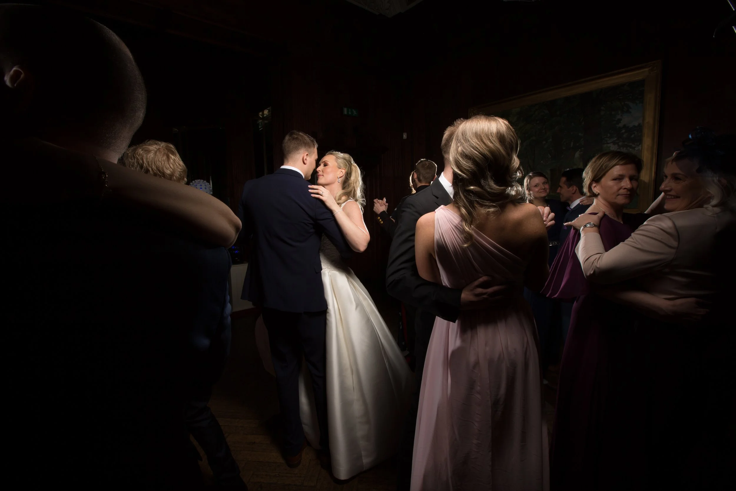 Couple dancing at a wedding reception, with guests watching and chatting in the background.