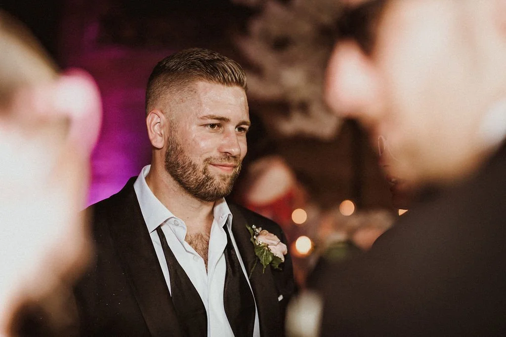 A man with a beard and suit looking at another person during a social event.