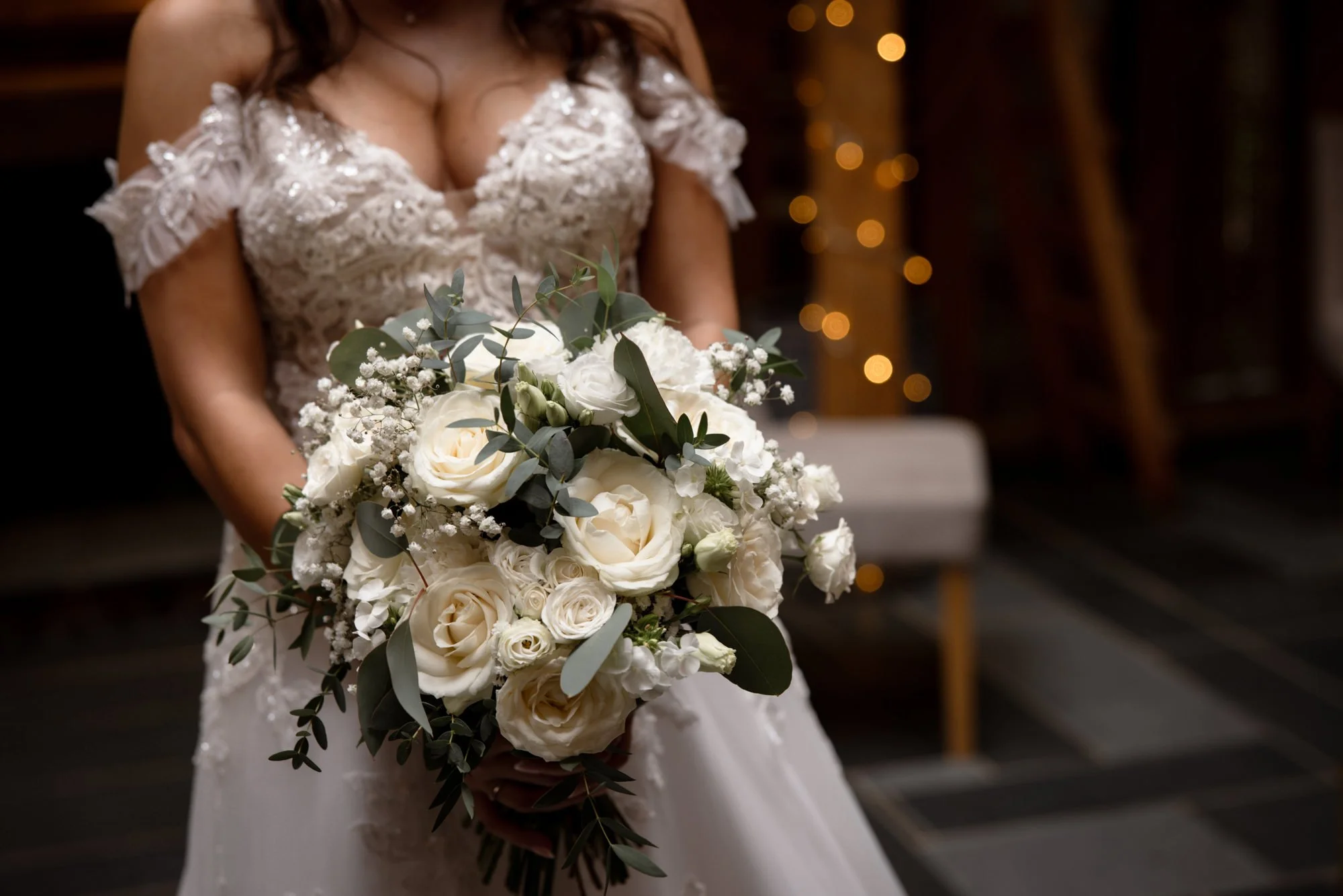 Bride in a lace wedding dress holding a bouquet of white roses, greenery, and baby's breath.