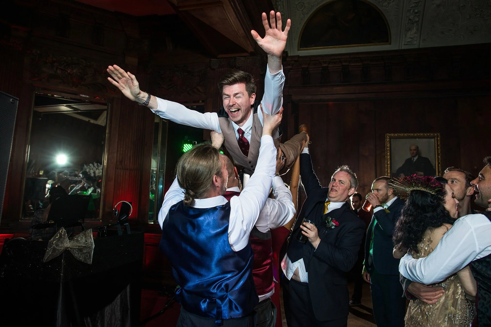 Groom party lift up a groomsman on the dancefloor into the air in a superman pose.