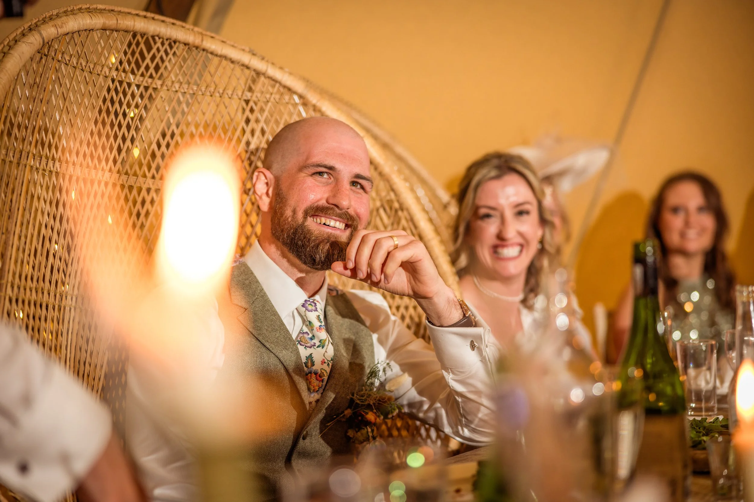People sitting at a table during a celebration, smiling and dressed formally, with warm lighting and decorative background.