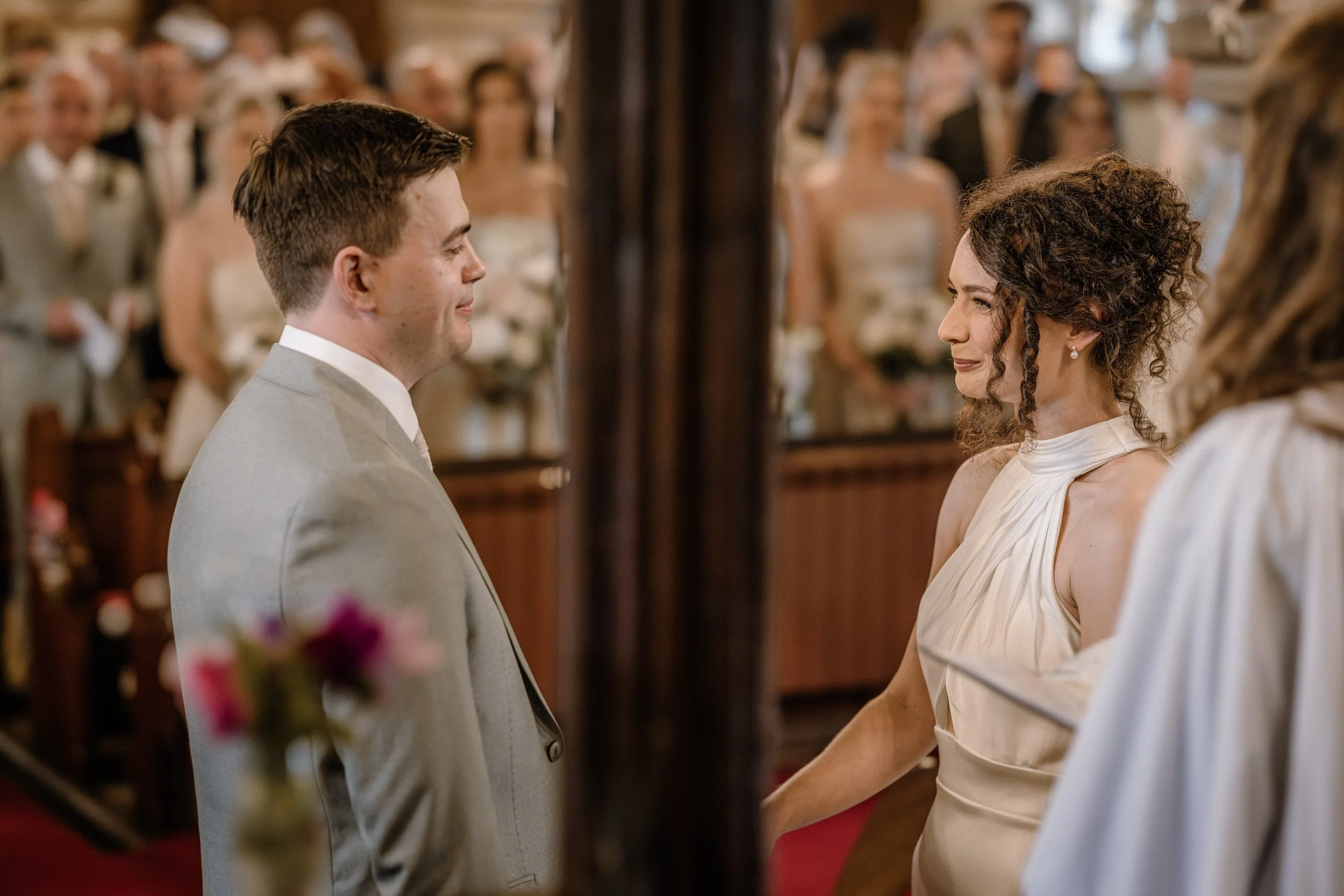 A bride and groom holding hands during their wedding ceremony in a church, with guests in the background.
