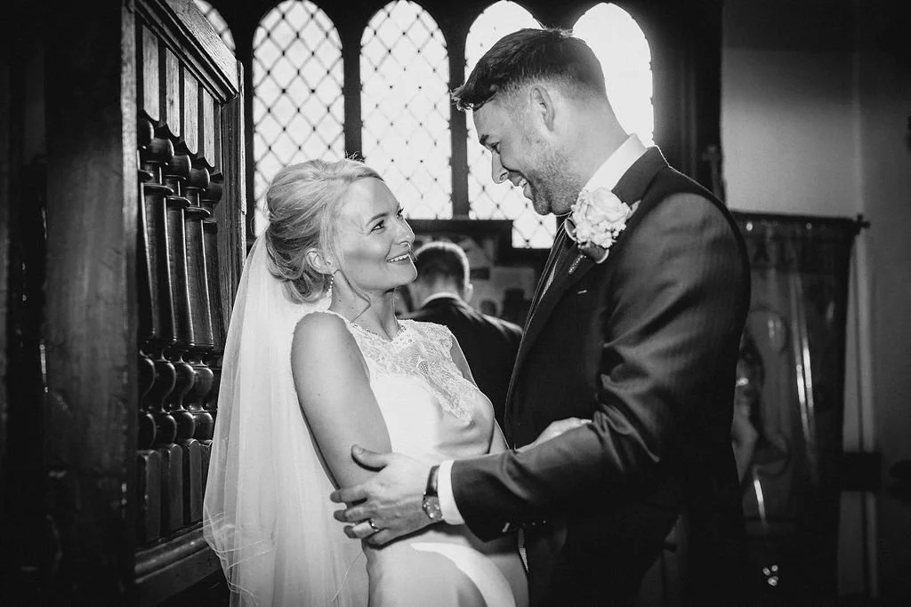 A bride and groom share a joyful moment during their wedding ceremony inside a church with stained glass windows.