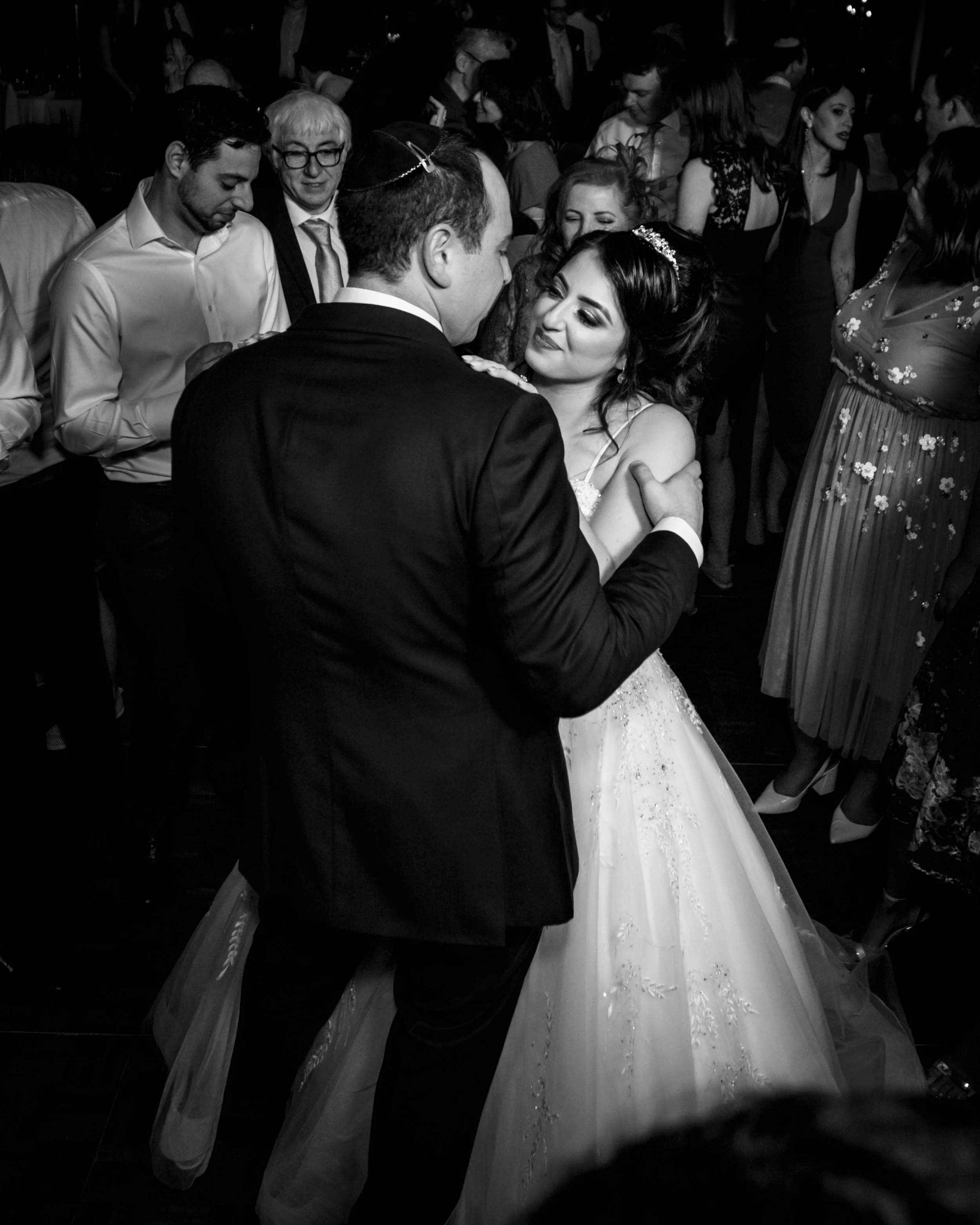 A bride and groom dancing at their wedding reception surrounded by guests.