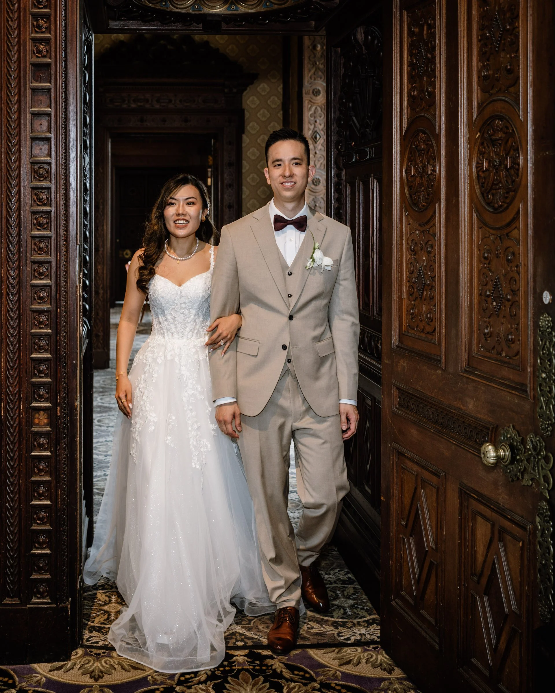 A bride and groom walking through a carved wooden doorway inside a decorated historic building.