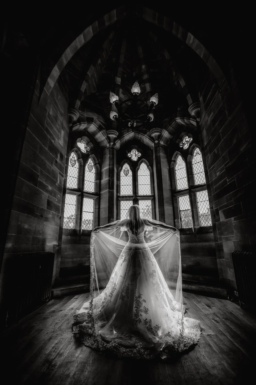 A bride standing in a Gothic-style church with large stained glass windows, wearing a wedding dress and holding the fabric of her gown