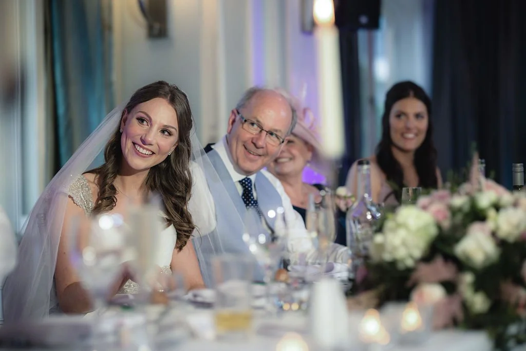 Wedding reception with bride, groom, and family members sitting at a decorated table.