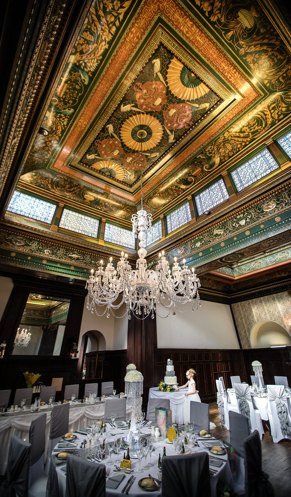 Little girl in white dress look at a wedding cake in huge room with ornate ceilings and chandelier