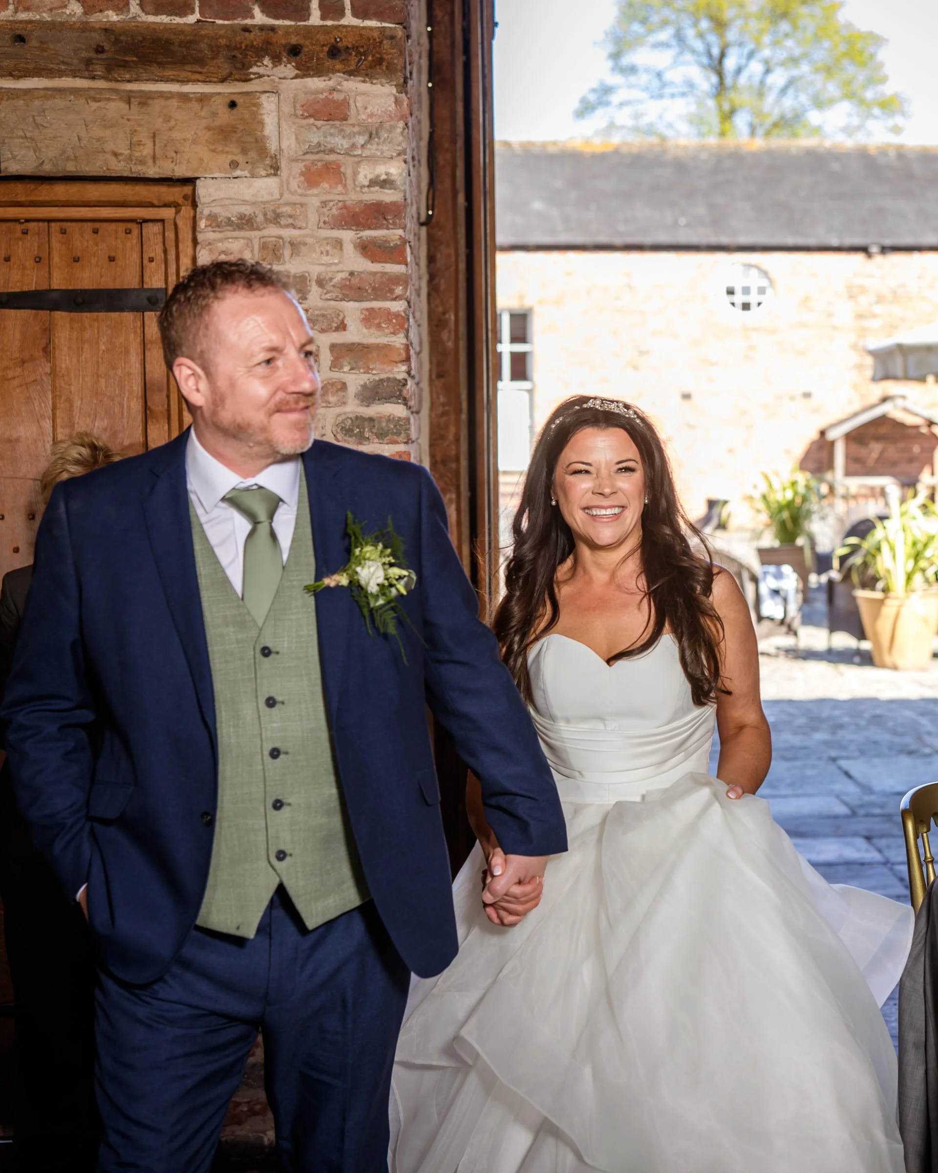 A bride and groom holding hands, standing inside a rustic venue with exposed brick walls and wooden accents, celebrating their wedding.