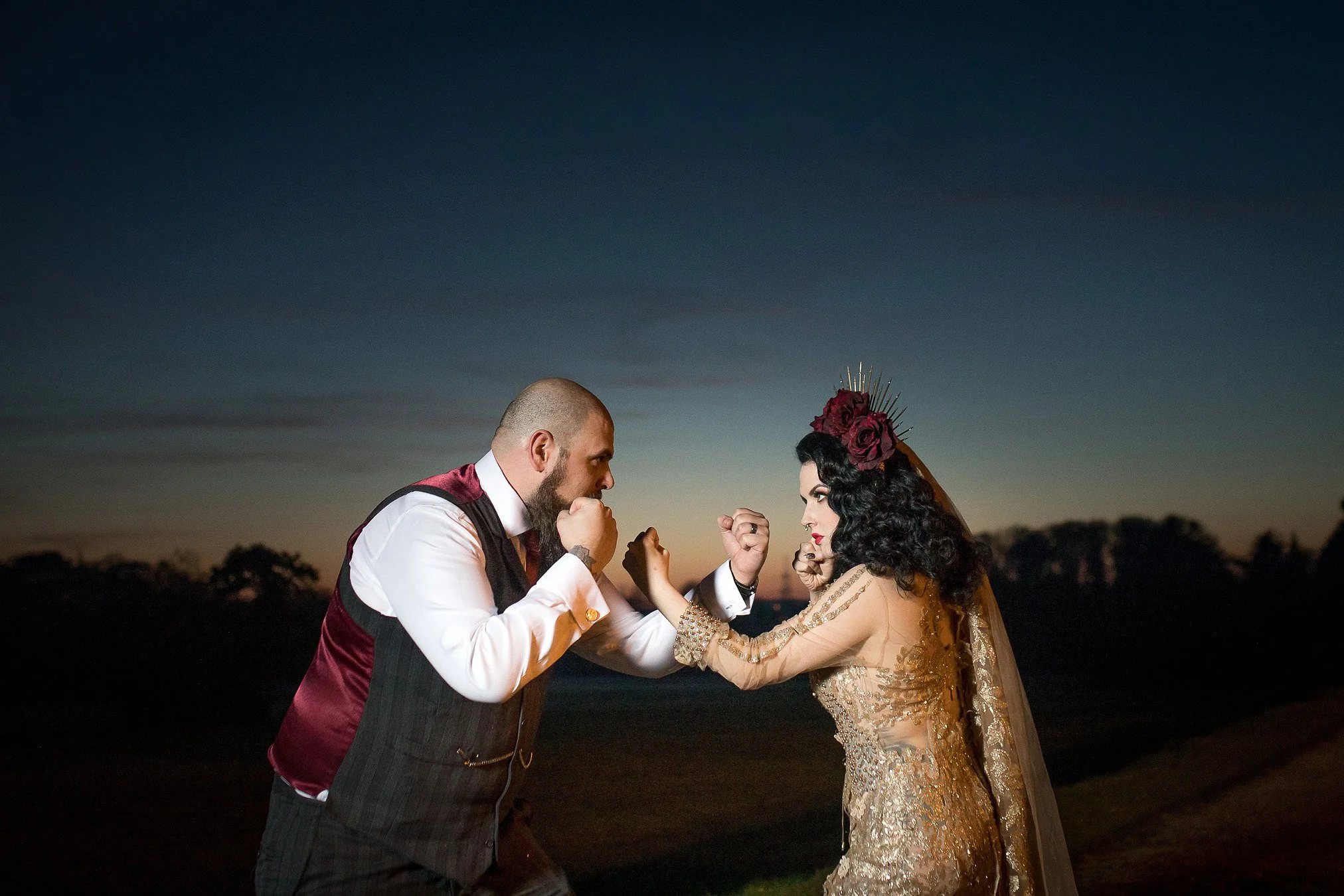 Bride in gold wedding dress and groom pose in a playful mock boxing stance for their evening portraits at Thornton Manor.