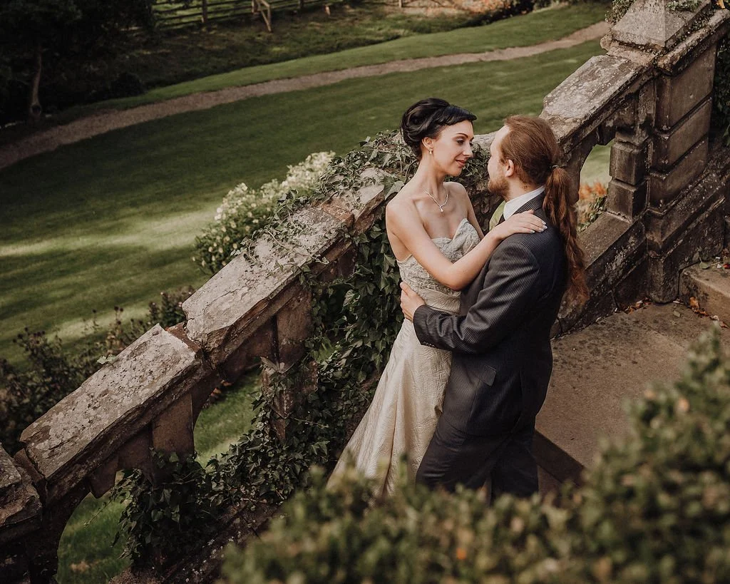 A bride and groom share an intimate moment on a stone staircase overlooking a lush garden.