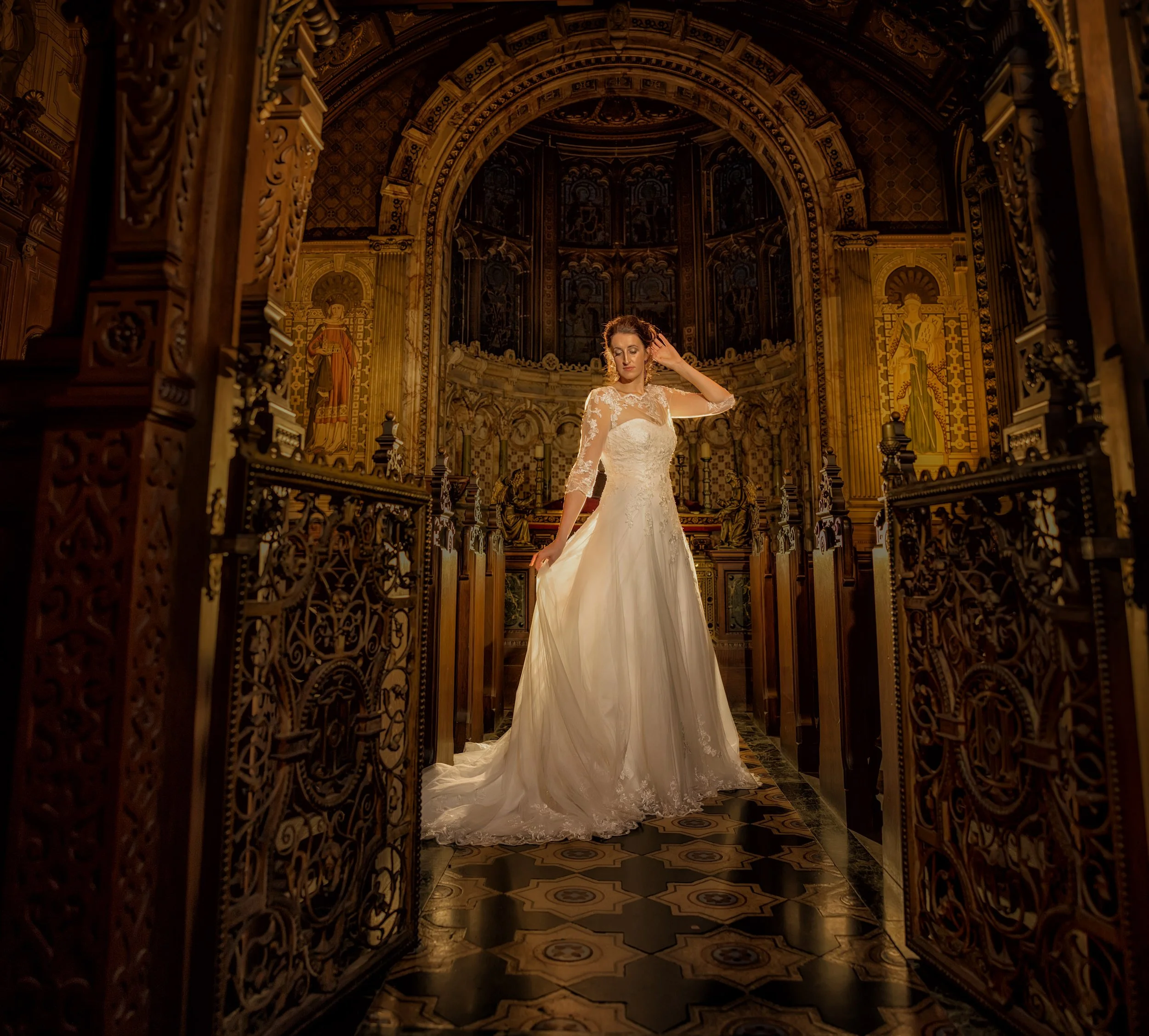 A woman in a wedding dress standing inside a church with ornate woodwork and religious artwork in the background.