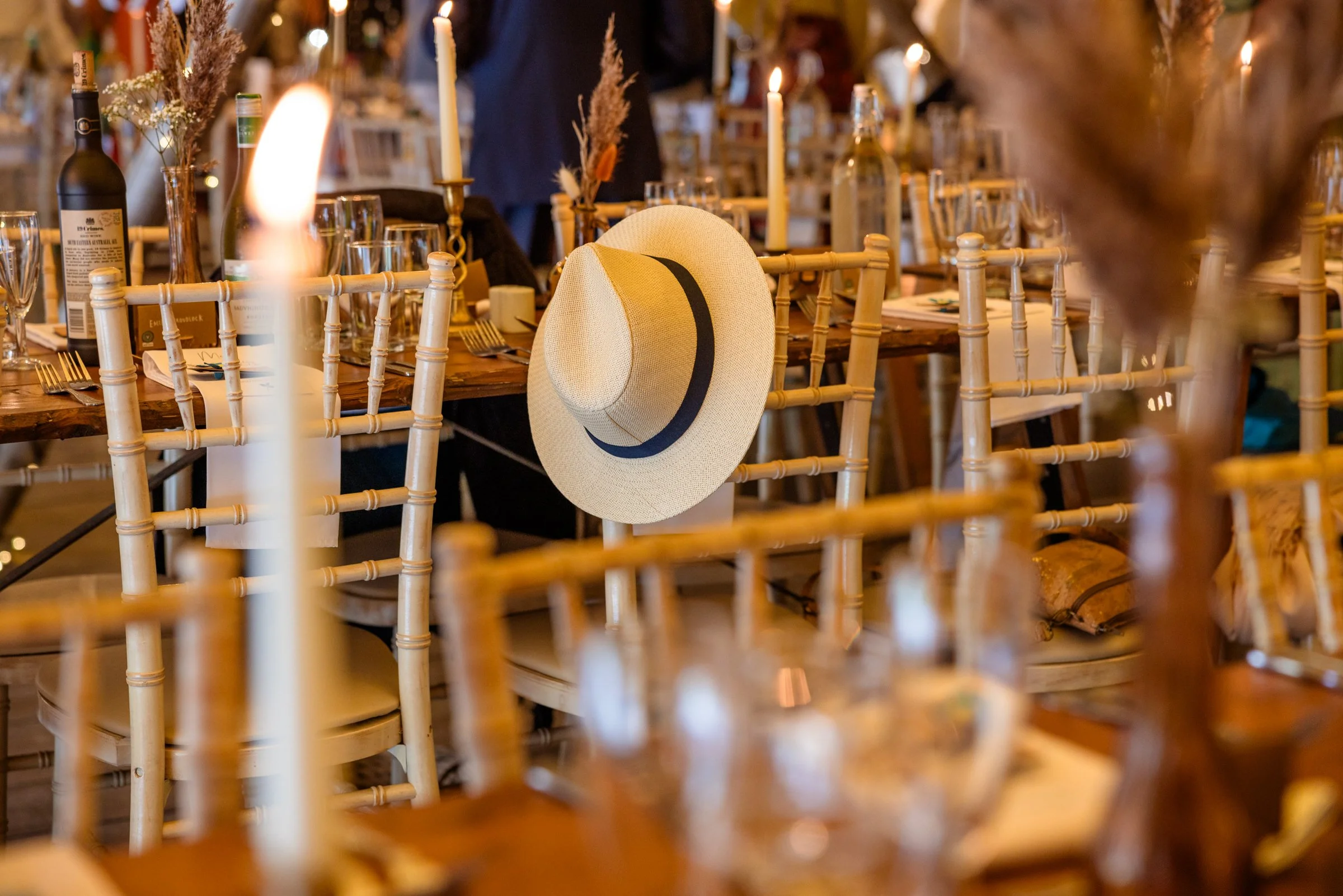 A hat hanging on the back of a chair at a decorated dining table with candles and wine bottles