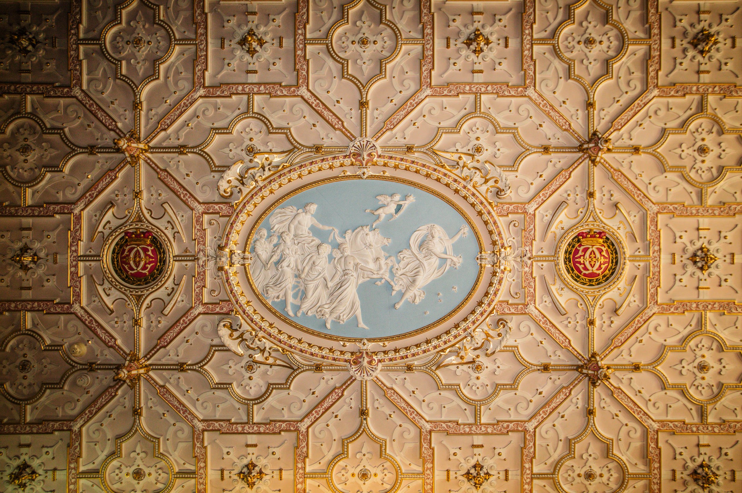 Ornate ceiling with intricate patterns, gold accents, and a central oval painting depicting mythological or historical figures and a chariot scene.