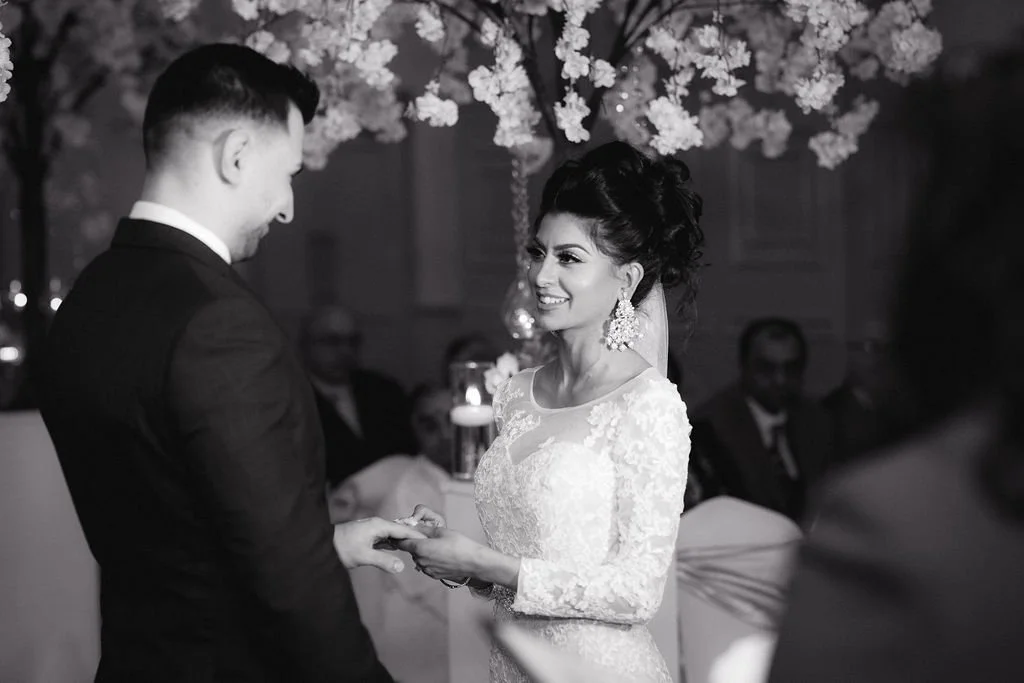 A bride and groom swapping rings during a wedding ceremony in a decorated venue.