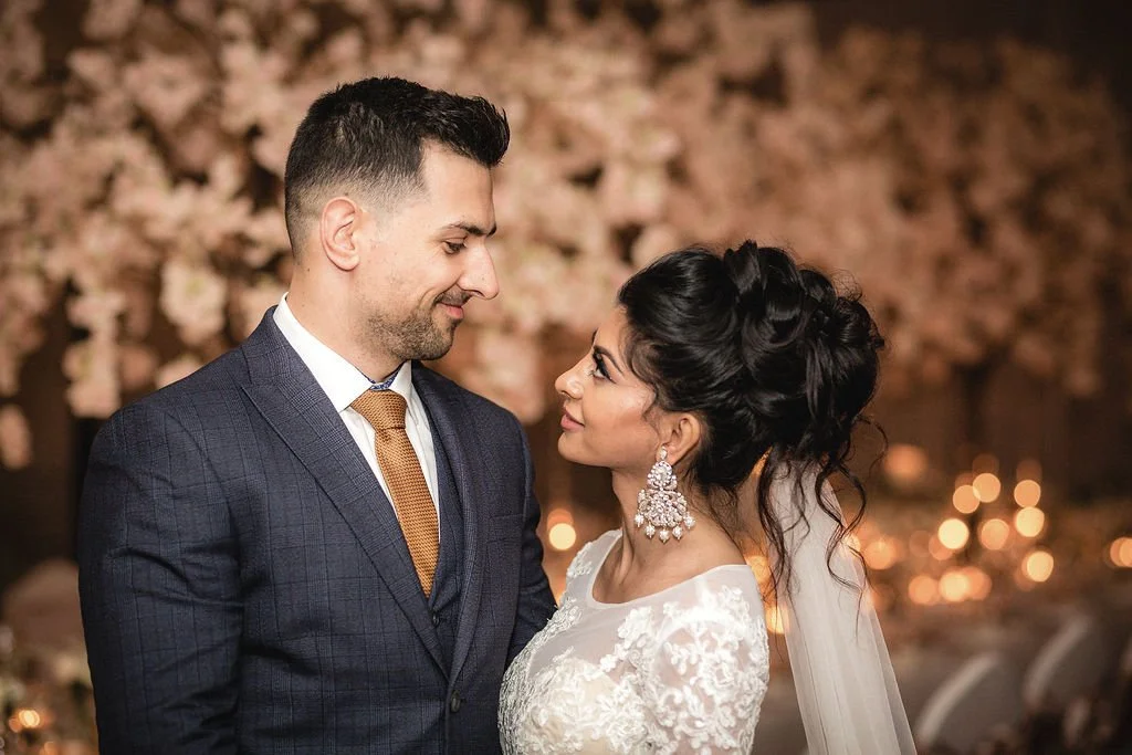 A bride and groom look at each other during their wedding reception, with floral decorations and soft lights in the background.