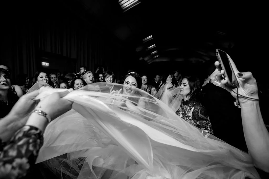 A bride surrounded by friends, with a wedding veil, in a joyful celebration.