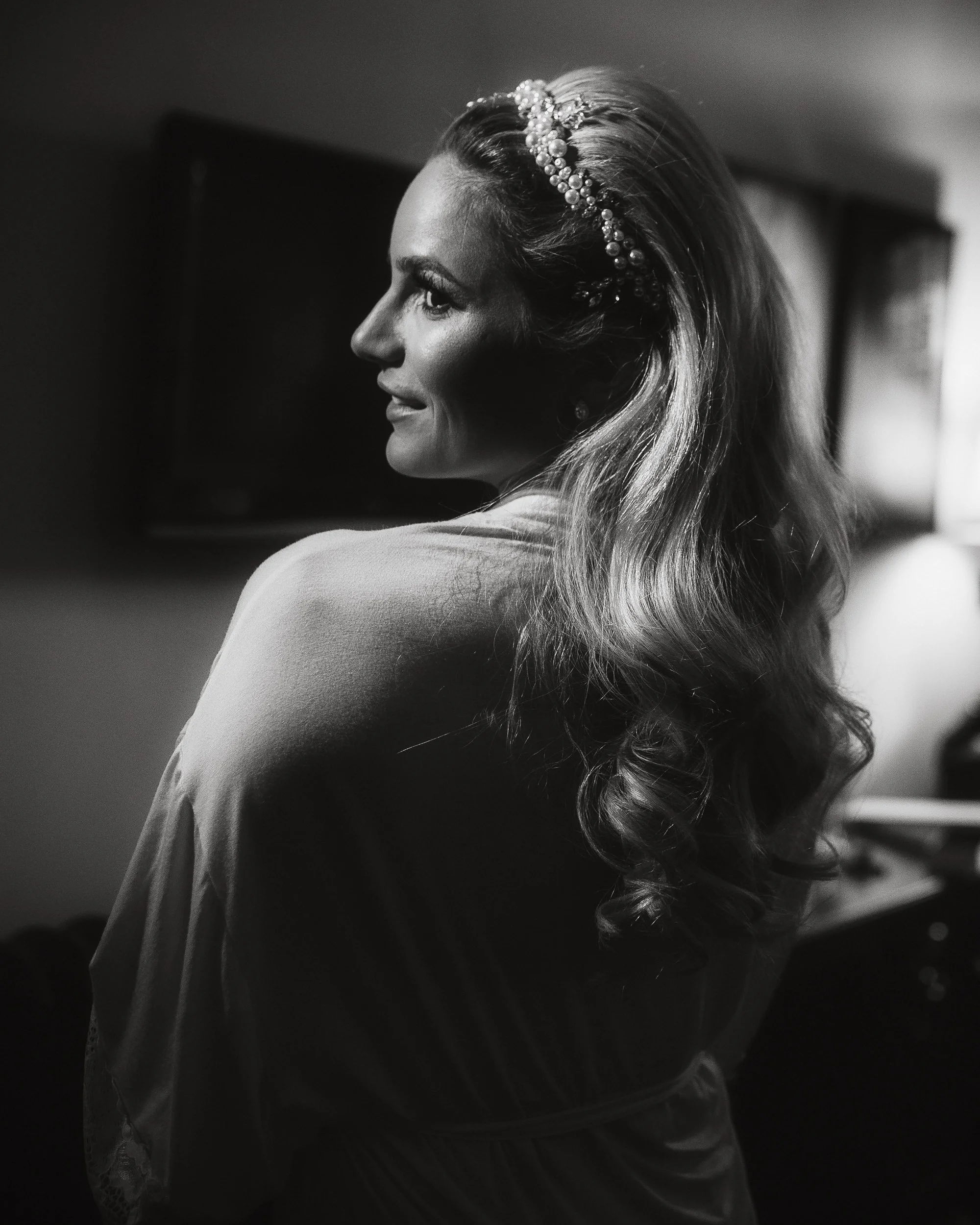 A woman with styled long hair wearing a pearl headband, looking to her left, in black and white.
