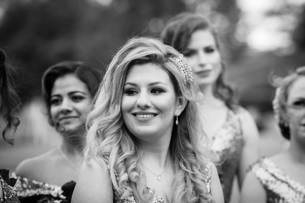 Black and white photo of a group of women dressed in elegant dresses, with the focus on a smiling woman with wavy hair and a decorative hair accessory.