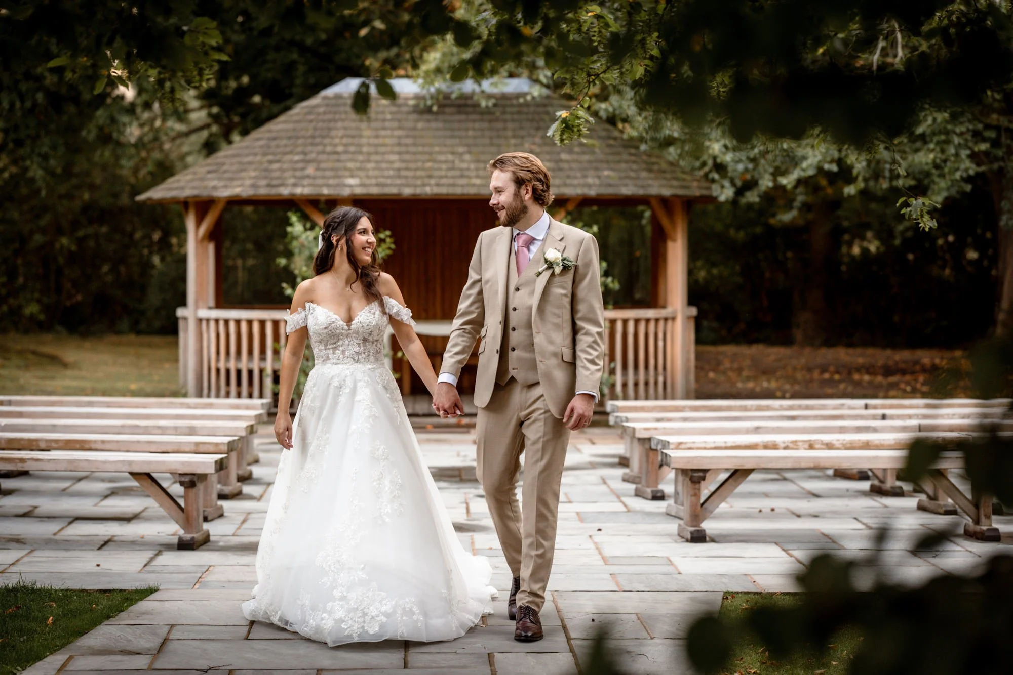 A bride and groom holding hands and smiling at each other outdoors during their wedding ceremony.