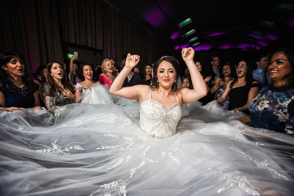 Bride dancing with her wedding dress surrounded by guests at a wedding reception.
