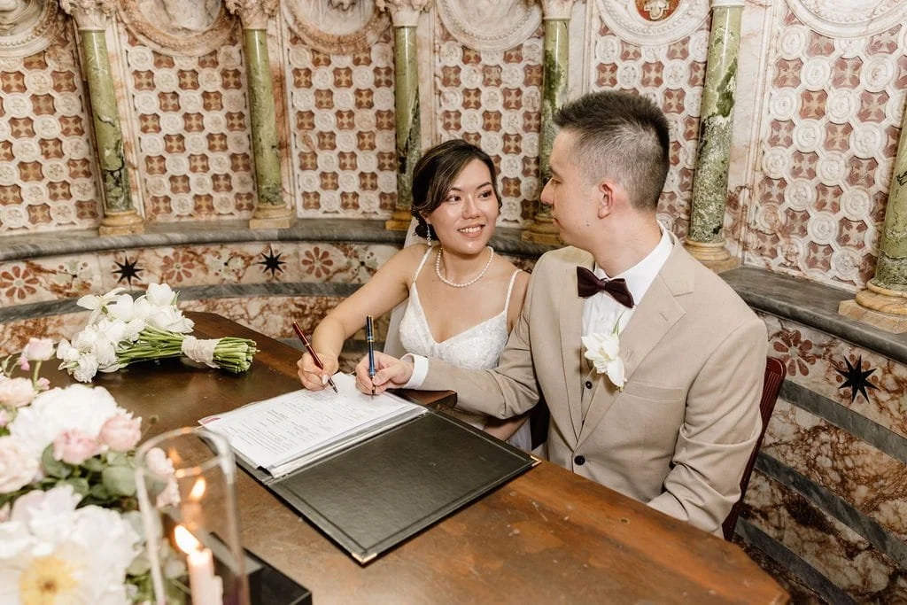 A bride and groom signing their marriage license at a decorated table with flowers and candles.
