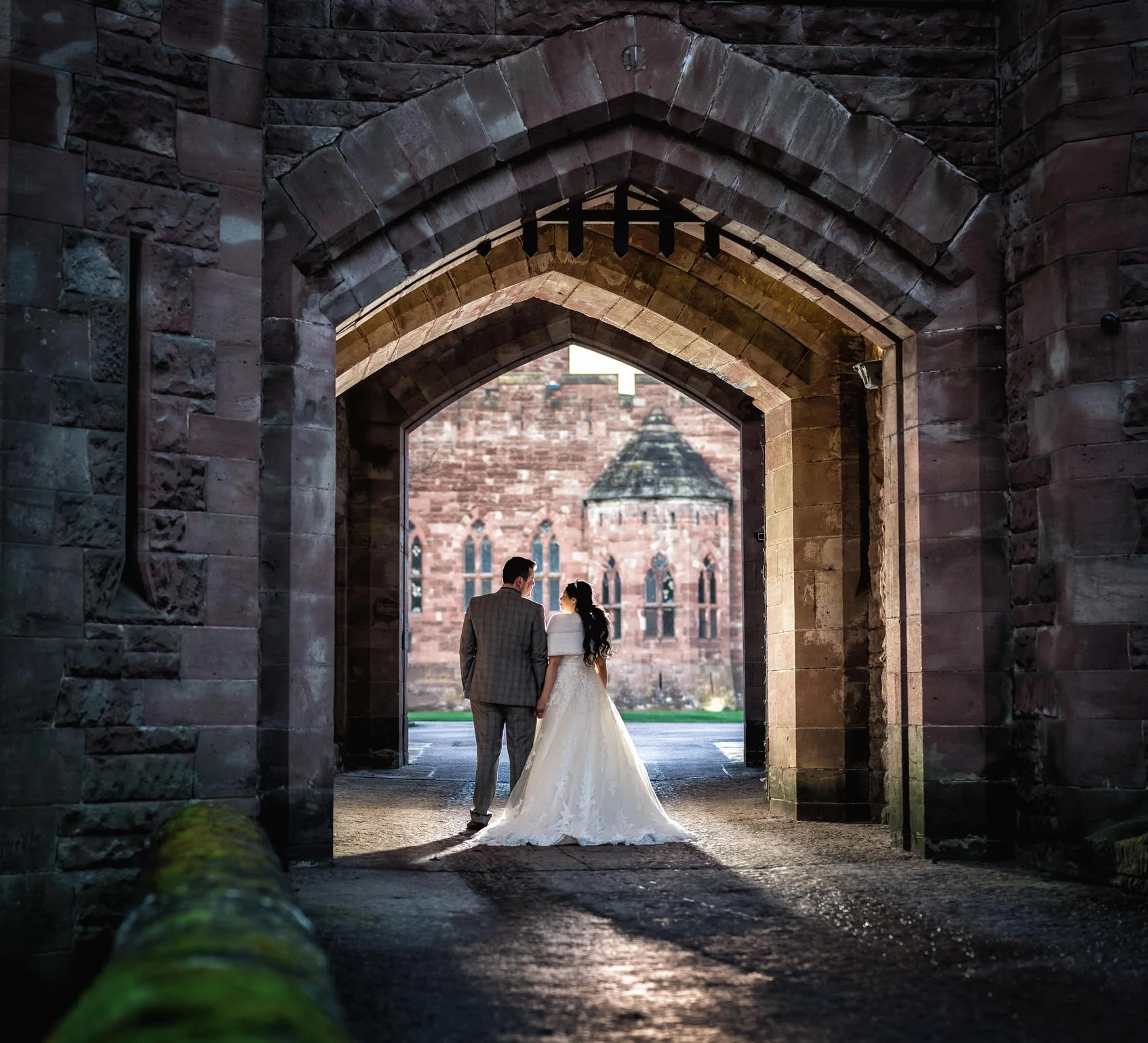 Bride and groom stand within the portcullis of a large stone walled castle