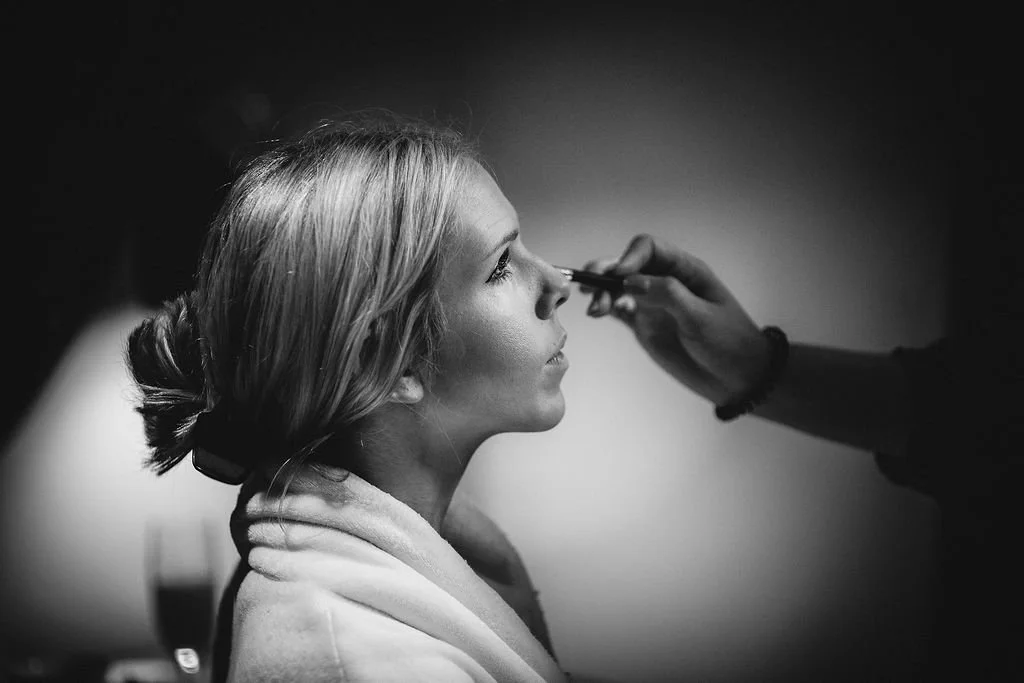 A woman getting her makeup done with a brush, profile view, black and white photo.
