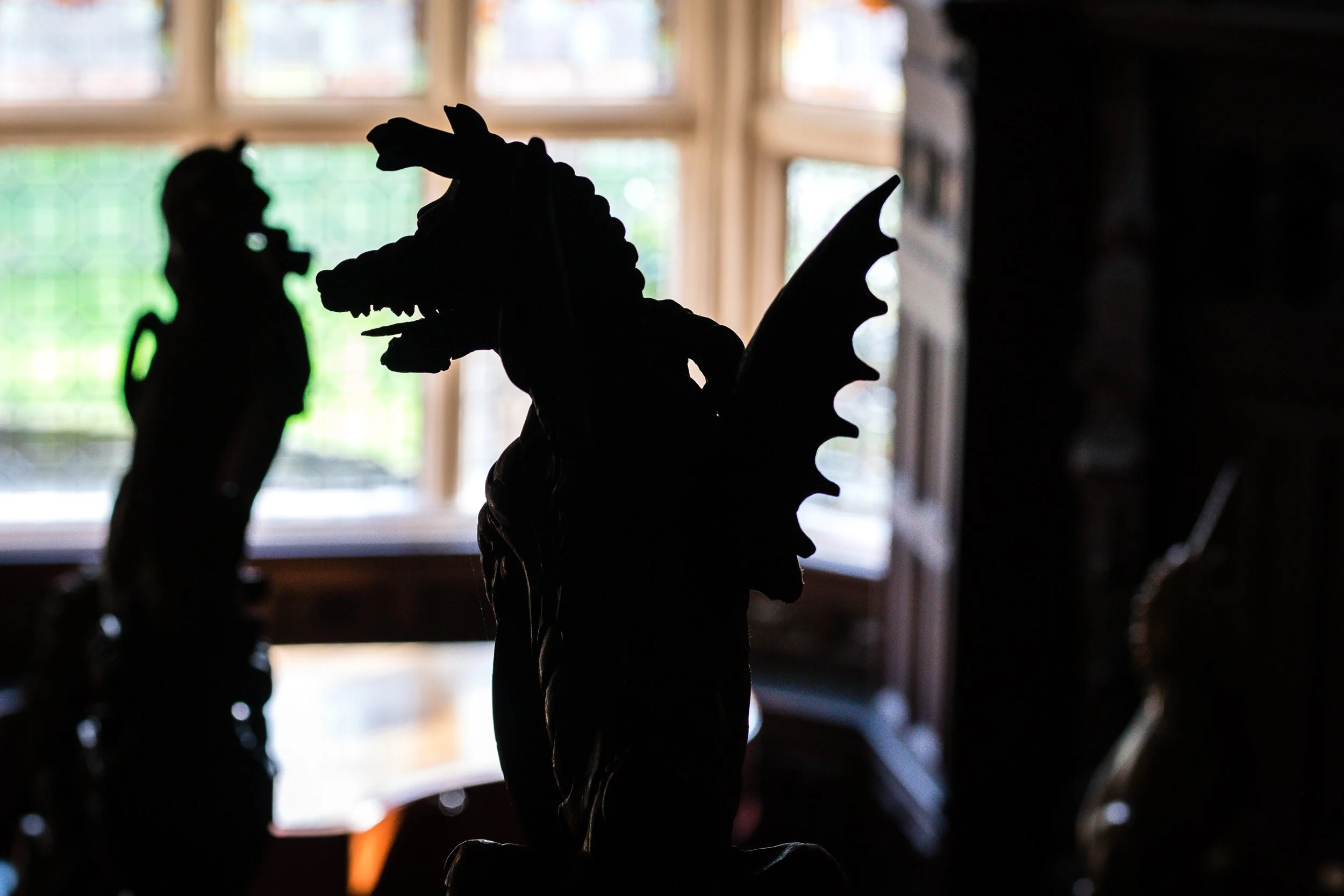 Silhouette of a dragon statue with wings, set against a window with natural light coming through.