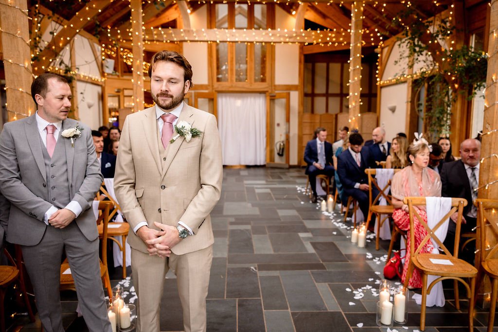 A wedding ceremony in a rustic wooden venue with string lights, candles, and guests seated on wooden chairs.