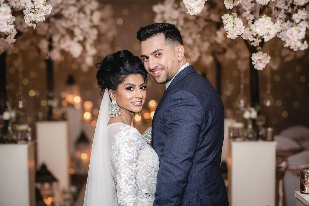 Bride and groom smiling at a wedding reception with floral decorations and soft lighting.