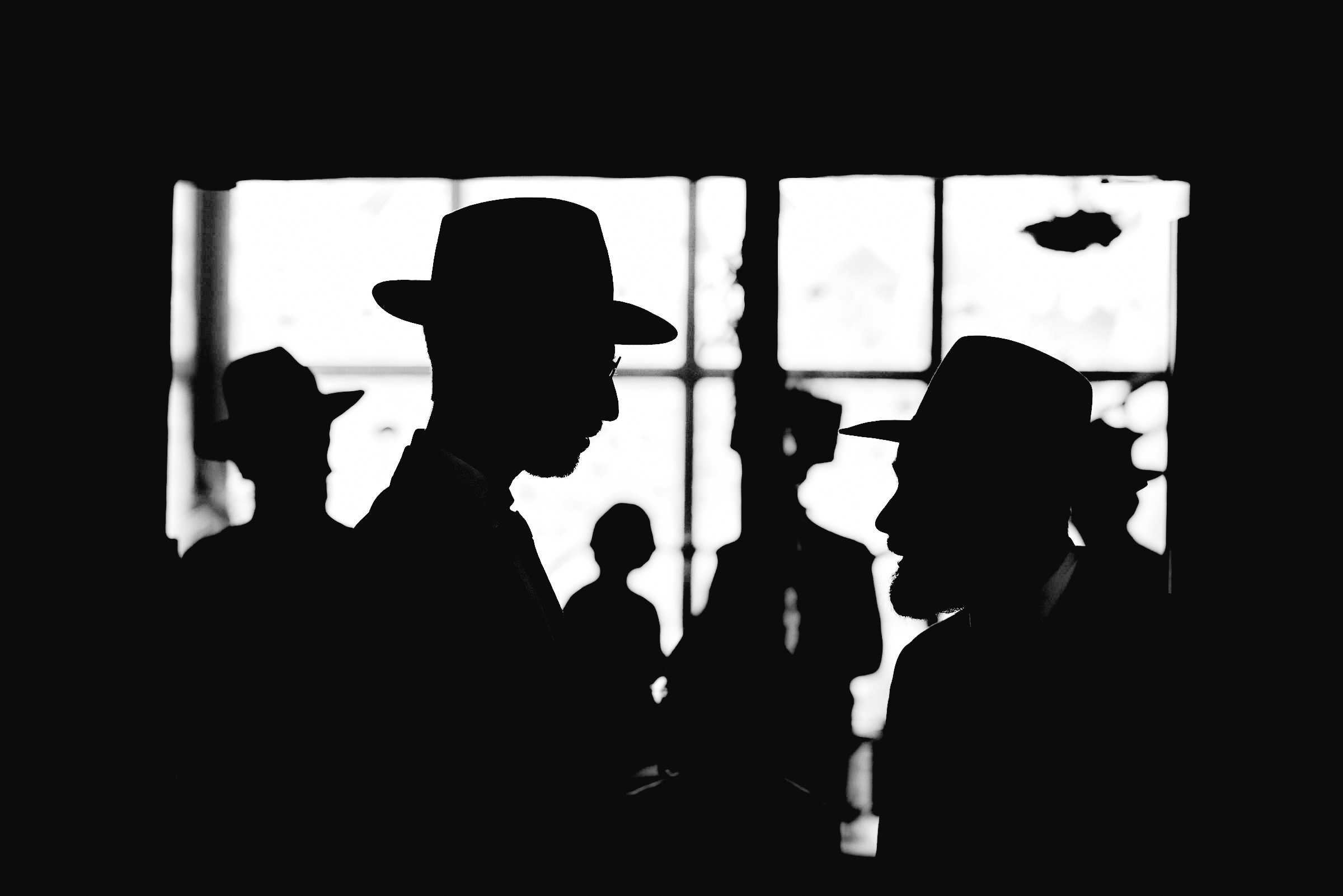 Silhouettes of several people wearing hats indoors with a bright window in the background.