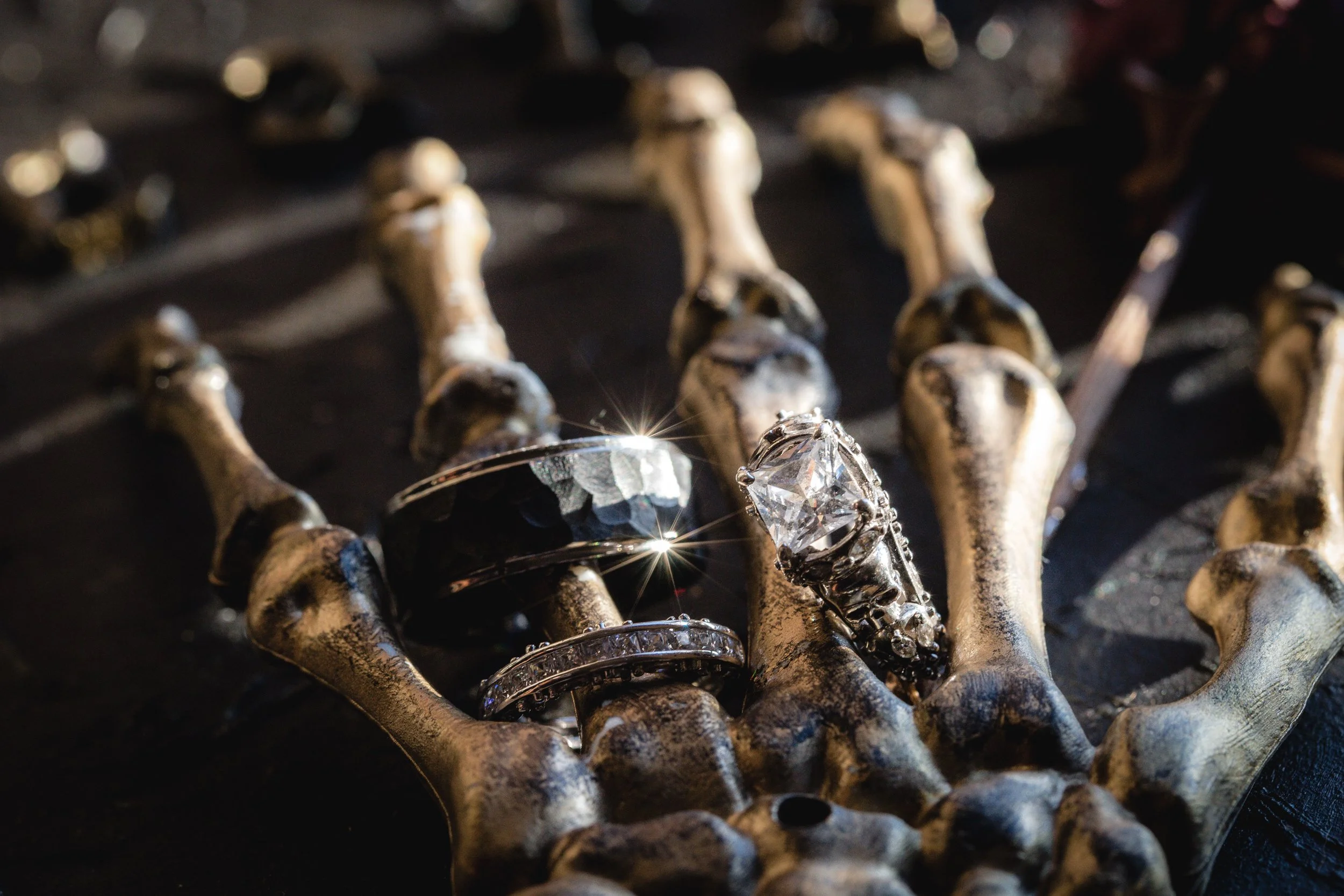 Jewelry pieces, including rings with large gemstones, placed on a metallic skeletal hand sculpture.