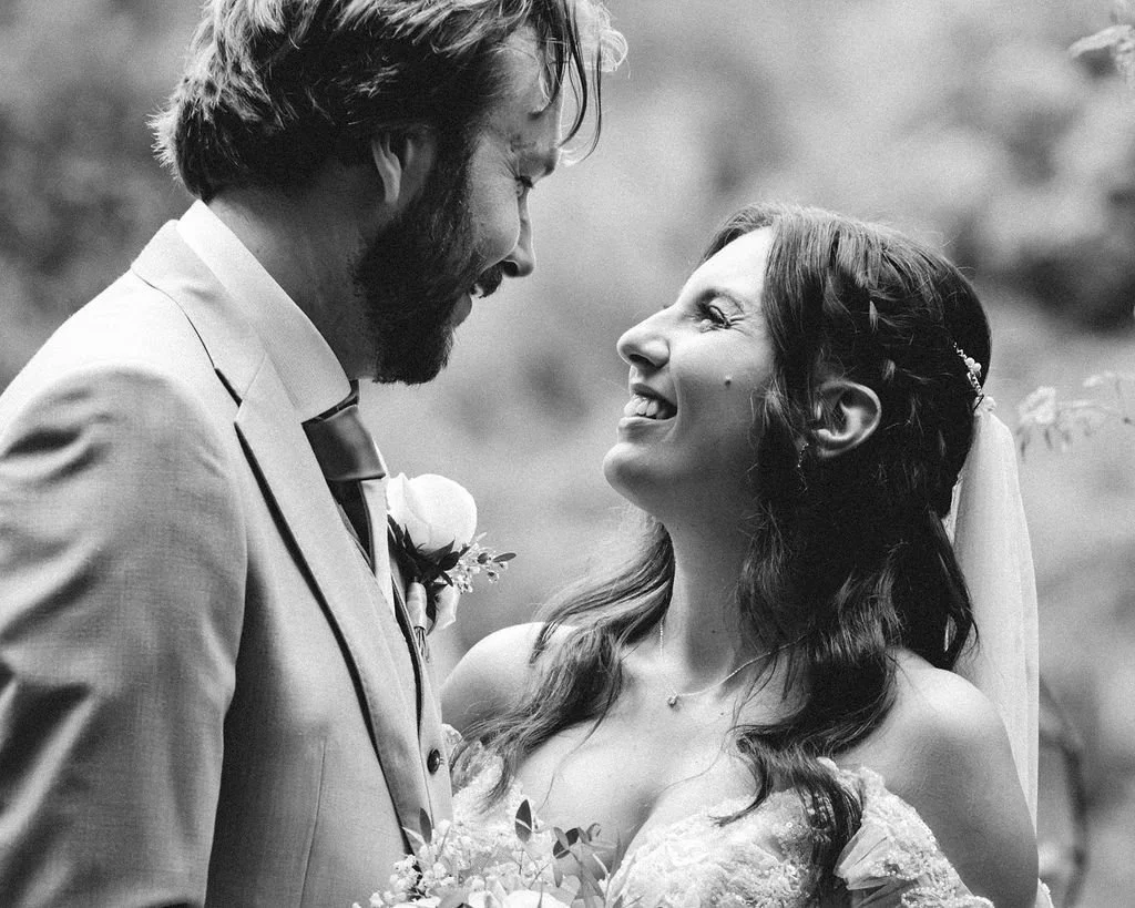 A black and white photo of a bride and groom looking at each other and smiling on their wedding day.
